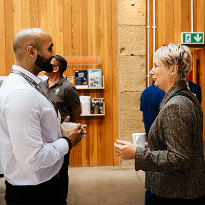 Group of people speaking to each other holding mugs of coffee or tea at EWIC.